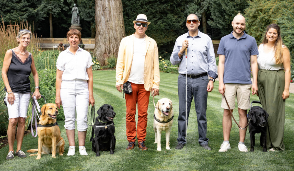 Gruppenfoto mit Blindenführunden auf grünem Rasen.
